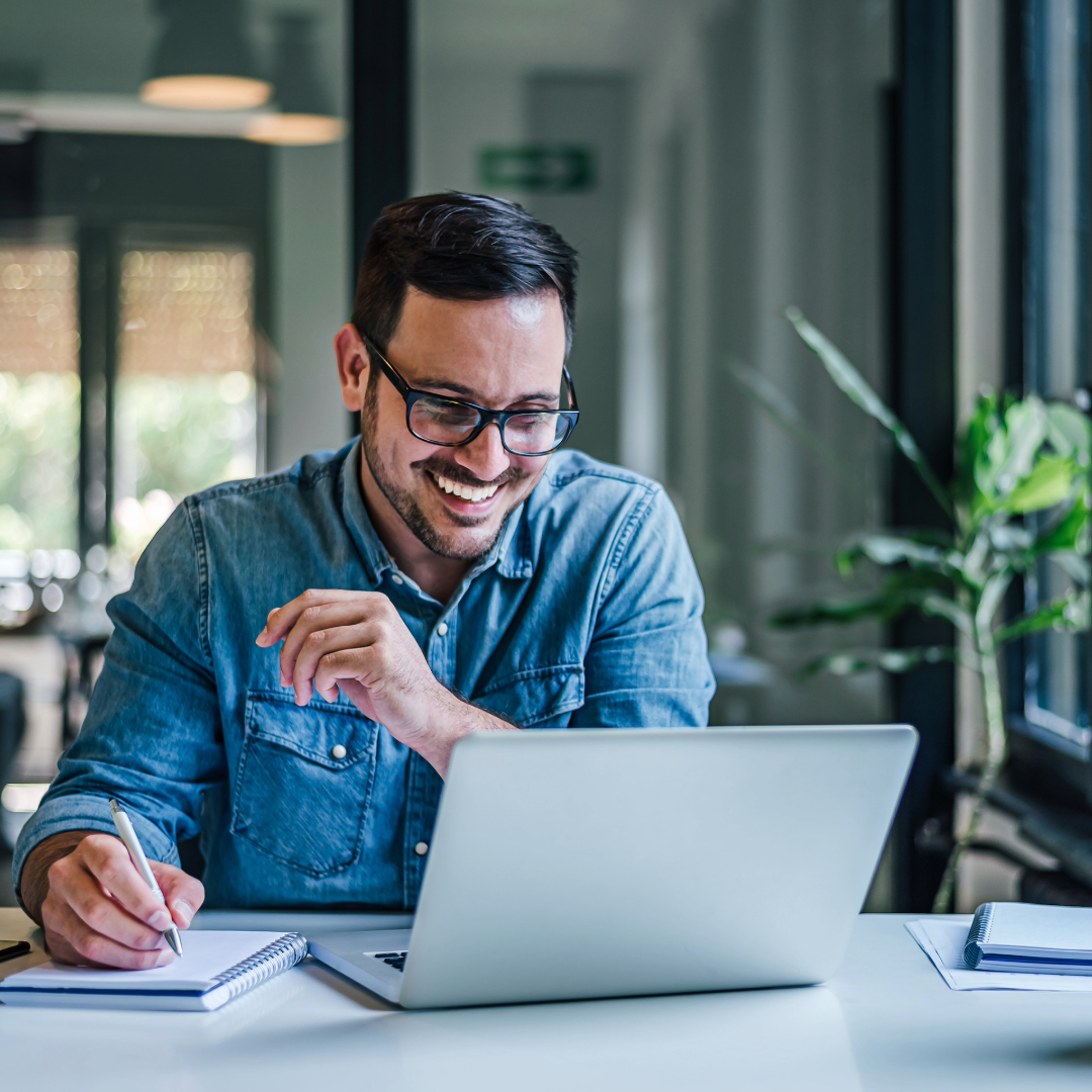 Man with eyeglasses working on a laptop and smiling.